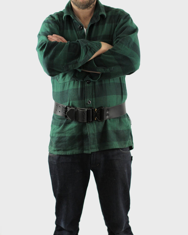 A person wearing a green checkered shirt and black pants, standing with arms crossed, featuring a black belt.