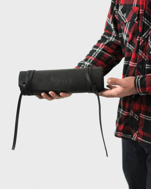 A person standing off to the side wearing a plaid shirt, holding a black leather chisel roll.