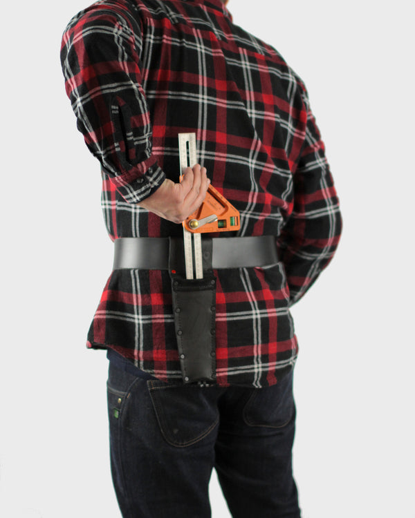 A person wearing a red and black plaid shirt and blue jeans has a combination square tool in a holster that is attached to a black belt.