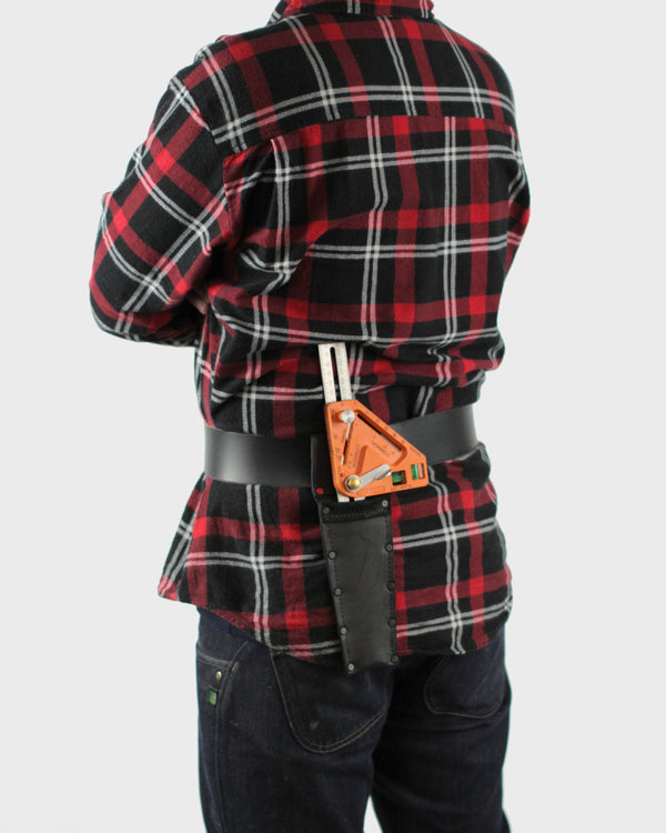 A person wearing a red and black plaid shirt and blue jeans has a combination square tool in a holster that is attached to a black belt.