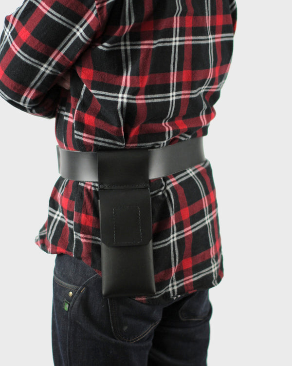 A person from behind, wearing a plaid shirt and a black belt, with a leather phone pouch on their belt.
