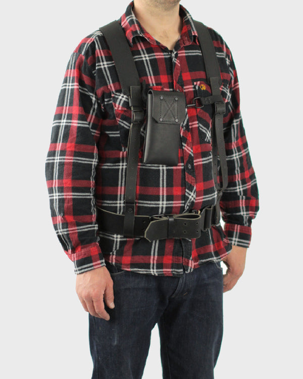 A person wearing a plaid shirt and a black belt and suspenders designed to hold a mobile phone.
